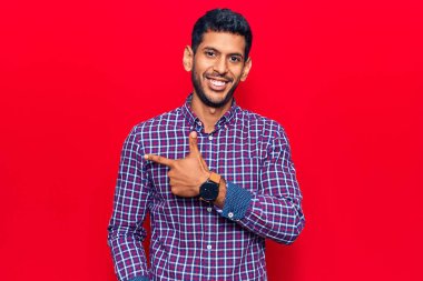 Gündelik kıyafetler giyen, neşeli gülümseyen, eli ve parmağı yanda olan genç bir latin adam. 