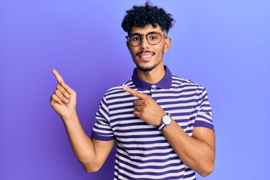 Genç Arap, sıradan kıyafetler ve gözlük takan, gülümseyen ve kameraya bakan yakışıklı bir adam.. 