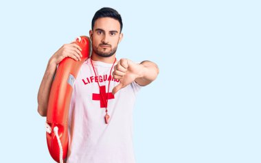 Genç yakışıklı adam cankurtaran üniforması giyiyor. Elinde kızgın bir yüz ifadesi var. Negatif işareti var. 