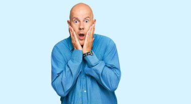 Orta yaşlı, kel, sıradan kıyafetler giyen, korkmuş ve şok olmuş, şaşırmış ve yüzünde elleri olan bir ifade. 