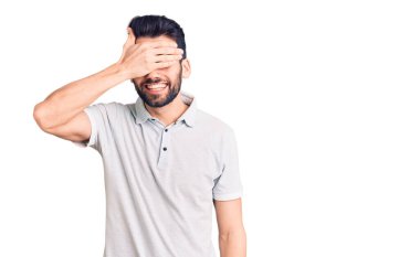 Sakallı, sıradan polo giyen, gülümseyen ve elleri yüzünde, şaşırtmak için gözlerini kapatan genç yakışıklı bir adam. kör kavram. 