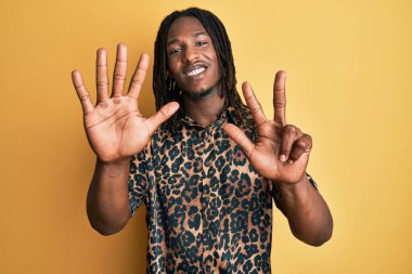 Saçlı, leopar desenli hayvan desenli tişörtlü Afro-Amerikan bir adam sekiz numaralı parmaklarını gösterip gösterirken kendinden emin ve mutlu gülümsüyor.. 