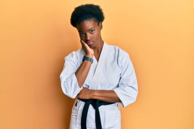 Karate kimonosu ve siyah kuşak giyen Afrikalı genç bir kız kollarını kavuşturup depresyondan sıkılmış ve yorgun görünüyor.. 