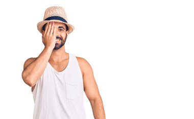 Gündelik yaz şapkası takan genç İspanyol bir adam bir gözünü eliyle kapatıyor, yüzünde kendine güvenen bir gülümseme ve sürpriz bir duygu var.. 