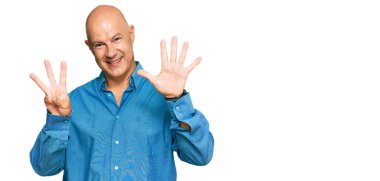 Orta yaşlı, kel, günlük kıyafetler giyen, 8 numaralı parmaklarıyla işaret eden, kendinden emin ve mutlu gülümseyen bir adam.. 