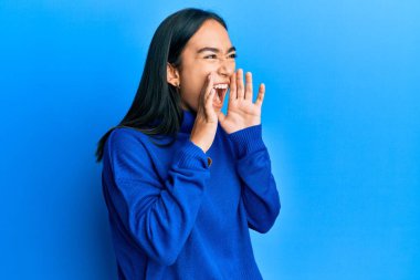 Sıradan bir kazak giyen genç Asyalı kadın elleri ağzında kızgın bir şekilde bağırıyor. 