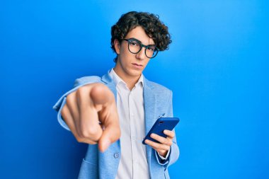Akıllı telefon kullanan, iş ceketi giyen, kamerayı işaret eden, kendine güvenen, ciddi görünen İspanyol bir genç. 