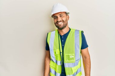 Sakallı, güvenlik kaskı takan ve yüzünde mutlu ve havalı bir gülümseme olan yakışıklı bir adam. şanslı kişi. 