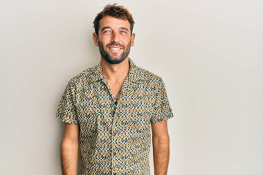 Yüzünde mutlu ve havalı bir gülümseme olan sıradan moda gömleği giyen sakallı yakışıklı bir adam. şanslı kişi. 