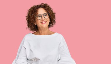 Güzel, orta yaşlı, normal kıyafetler ve gözlük takan, yüzünde gülümsemeyle yan yana bakan olgun bir kadın, doğal bir ifade. Kendinden emin gülen. 