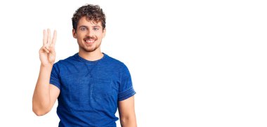 Kıvırcık saçlı, rahat giyinen, üç numaralı parmaklarıyla işaret eden, kendinden emin ve mutlu gülümseyen genç yakışıklı bir adam.. 
