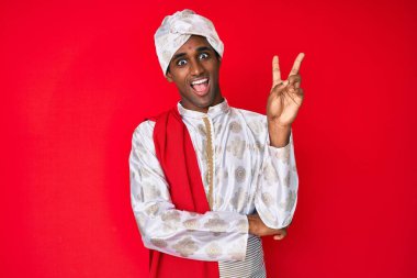 Sherwani sari giysisi giyen yakışıklı Hintli adam kameraya gülümseyip zafer işareti yapıyor. İki numara.. 