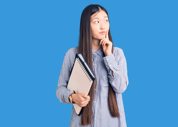 Young Beautiful Chinese Woman Holding Notebook Serious Face Thinking Question — Stock Photo, Image