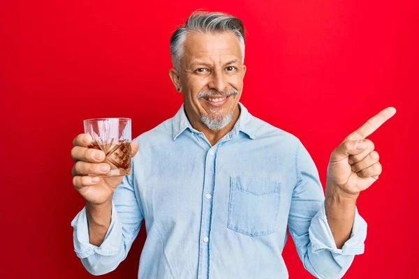 Medelålders Gråhårig Man Dricker Glas Whisky Leende Glad Pekar Med — Stockfoto