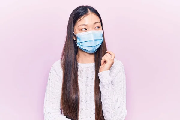 Νεαρή Όμορφη Κινέζα Γυναίκα Που Φοράει Ιατρική Μάσκα Σκέφτεται Συγκεντρωμένα — Φωτογραφία Αρχείου