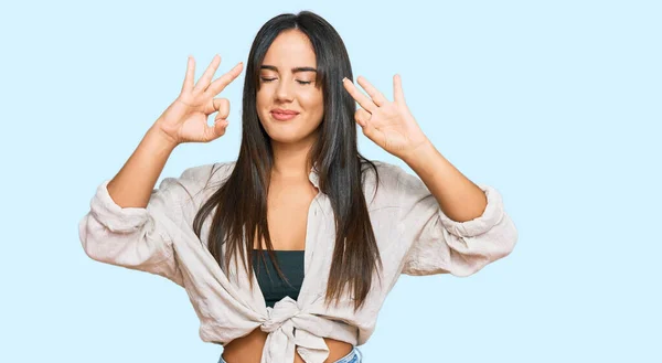 若い美しいヒスパニック系の女の子がリラックスしたカジュアルな服を着て 目を閉じて指で瞑想ジェスチャーを行う笑顔 ヨガのコンセプト — ストック写真