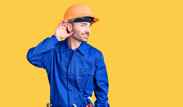 噂やゴシップに耳を傾け手で笑みを浮かべて労働者の制服を着た若いヒスパニック系の男 聴覚障害の概念 — ストック写真