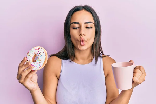 年轻的黑发女人吃甜甜圈 喝咖啡 用嘴和眼神做鱼脸 疯狂而滑稽 — 图库照片