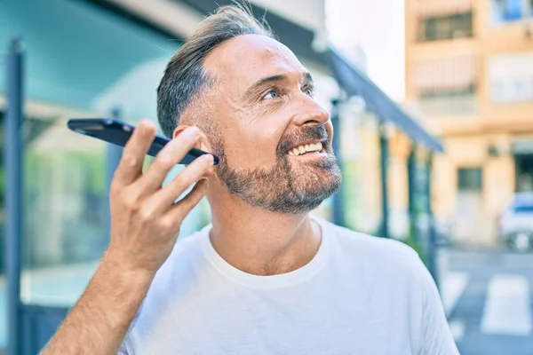 Красивый Мужчина Средних Лет Улыбающийся Счастливым Слушая Аудиосообщение Используя Смартфон — стоковое фото