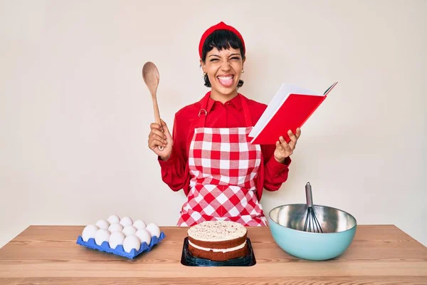 Piękna Brunetka Kobieta Gotowanie Ciasto Czytanie Receptur Książki Wystające Język — Zdjęcie stockowe