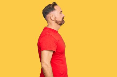 Yakışıklı, orta yaşlı, sıradan kırmızı tişört giyen, rahat bir görünüm takınan, kendine güvenen, güler yüzlü bir adam.. 