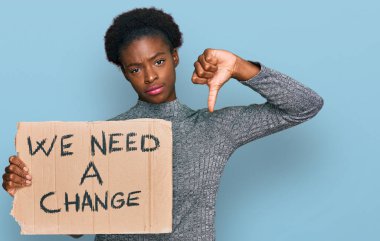 Genç Afro-Amerikan kızı elinde tutuyor. Değişim afişine ihtiyacımız var. Kızgın suratlı, olumsuz işaretli, başparmakları aşağıda, reddedilme kavramlı. 