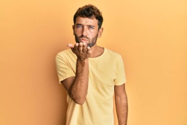 Sarı arka planda sıradan sarı tişörtler giyen sakallı yakışıklı bir adam. Kameraya bakıp havada el sallayan bir öpücük veriyor. Güzel ve seksi. aşk ifadesi. 