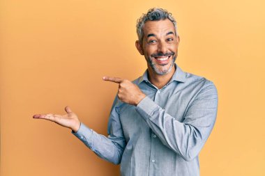 Orta yaşlı, gri saçlı, sıradan kıyafetler giyen bir adam kameraya hayret ediyor ve gülümsüyor.. 