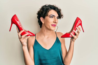 Genç adam zarif kırmızı topuklu ayakkabılar giyerek makyaj yapıyor. Gülümsüyor ve yan tarafa bakıyor.. 