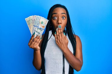 Genç Afro-Amerikalı kadın elinde dolarlarla ağzı kapalı, şok olmuş ve hata yapmaktan korkan. şaşırmış ifade 