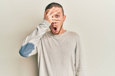 Sıradan bir kazak giyen İspanyol genç adam şok içinde yüzünü ve gözlerini eliyle kapatıyor, parmaklarından korkuyla bakıyor. 