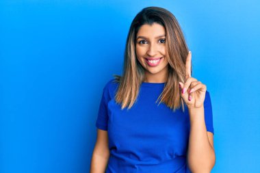 Güzel esmer kadın, günlük mavi tişört giyiyor. Bir fikir veya soruyla gülümsüyor. Mutlu bir yüzle işaret ediyor. 