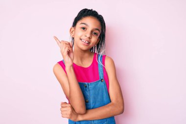 Saçları örgülü, pembe arka planda, yüzünde kocaman bir gülümsemeyle, elleri ve parmaklarıyla kameraya bakan Afro-Amerikan bir kız çocuğu.. 