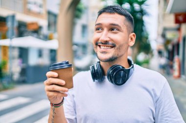 Kulaklık takan genç İspanyol adam şehir caddesinde kahve içiyor..
