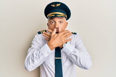 Yakışıklı, orta yaşlı, uçak pilotu üniforması giyen olgun bir adam ağzını yanlışlıkla ellerle kapatırken şok geçirdi. gizli kavram. 