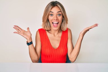 Güzelim beyaz kadın gündelik giysiler içinde masaya oturmuş zaferi kutluyor mutlu bir gülümseme ve ellerini kaldırarak kazanan bir ifadeyle. 