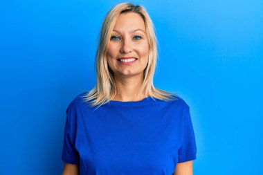 Orta yaşlı, beyaz, sıradan mavi tişörtlü, yüzünde mutlu ve havalı bir gülümseme olan bir kadın. şanslı kişi. 