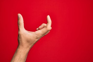 Kafkasyalı genç adam parmaklarını izole edilmiş kırmızı arka plan üzerinde gösteriyor ve görünmez şeyi alıyor, parmakları boşluk gösteren nesneleri tutuyor.