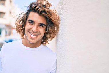 Genç yakışıklı İspanyol gülümseyen mutlu bir adam şehrin duvarına yaslanıyor.