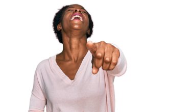 Gündelik giysiler giymiş genç Afro-Amerikalı kız sana gülüyor, kamerayı işaret ediyor, yüzünü gösteriyor, utanç ifadesi. 