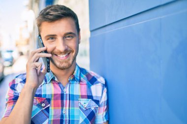 Genç beyaz adam gülümsüyor. Şehirdeki akıllı telefondan konuşuyor..