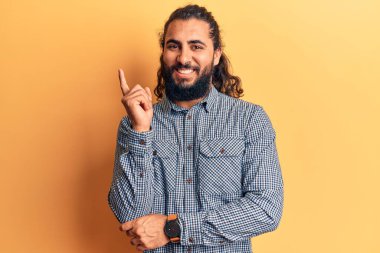 Gündelik giysiler giyen genç Arap adam gülümsüyor mutlu bir şekilde elini ve parmağını yana uzatıyordu. 