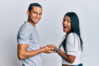 Young latin couple wearing casual clothes pointing aside with hands open palms showing copy space, presenting advertisement smiling excited happy 