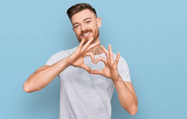 Genç, kızıl saçlı, sıradan gri tişörtlü aşık gülümseyen, elleriyle kalp sembolü yapan bir adam. romantik kavram. 