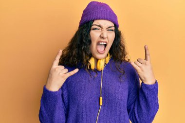 Kıvırcık saçlı, müzik dinleyen, kulaklık takan çılgın ifadeli, elleri havada rock sembolü yapan genç esmer kadın. Müzik yıldızı. ağır kavram. 