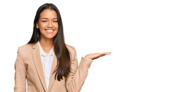 Güzel İspanyol kadın iş ceketi giyiyor neşeli bir şekilde gülümsüyor ve avuç içiyle kameraya bakıyor.. 