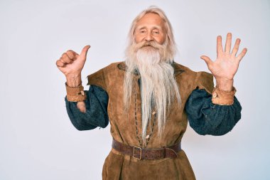 Gri saçlı, uzun sakallı, Viking kostümü giyen, 6 numaralı parmaklarını gösterip gülümseyen, kendinden emin ve mutlu yaşlı bir adam.. 