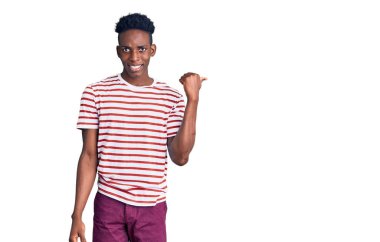 Genç Afro-Amerikalı günlük kıyafetler giymiş mutlu yüzüyle gülümseyen ve başparmağıyla yüzünü gösteren bir adam.. 