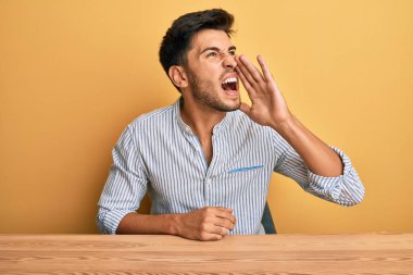 Gündelik giysiler giymiş genç yakışıklı adam masaya oturmuş el ele tutuşmuş bağırıyor ve çığlık çığlığa bağırıyordu. iletişim konsepti. 