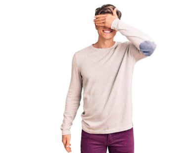 Gündelik kıyafetler giyen, gülümseyen ve gülümseyen genç yakışıklı adam şaşırmak için gözlerini kapatıyor. kör kavram. 